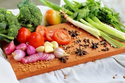 Gemüse wie Brokkoli, Tomaten, Lauch, Zwiebeln, Knoblauch und Anissterne und Pfefferkörner liegen auf einem Holzschneidebrett 